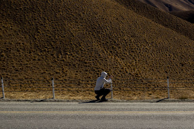 Rear view full length of man crouching by mountain on road
