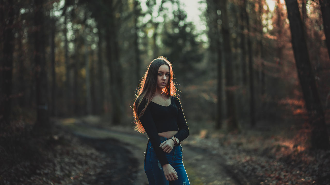 tree, forest, land, one person, plant, leisure activity, nature, real people, lifestyles, woodland, focus on foreground, standing, young women, casual clothing, young adult, three quarter length, front view, women, trunk, outdoors, beautiful woman, hairstyle