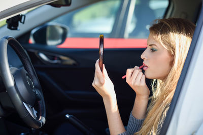 Young woman applying lipstick in car