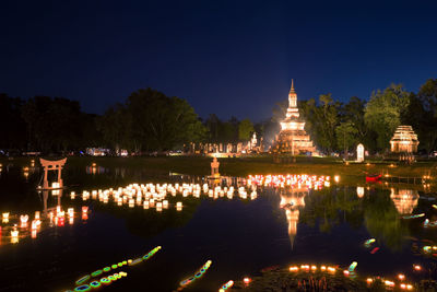 Illuminated building by lake against sky at night