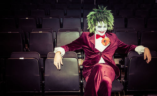 Portrait of man wearing clown costume sitting on chair