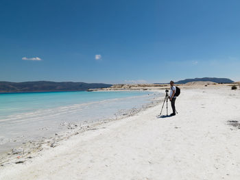 Man with camera standing at beach against sky