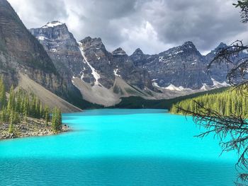 Scenic view of turquoise coloured lake by mountains against sky