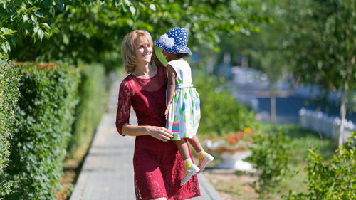 Mother carrying daughter at park on sunny day