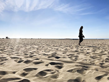 Side view of silhouette woman walking at beach against blue sky