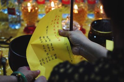 Woman, rear view, holding a yellow prayer card and some incenses. in a taoist temple