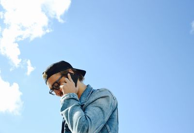 Low angle view of man talking on mobile phone against blue sky