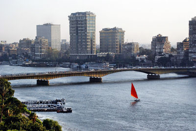 Bridge over river by buildings in city against sky