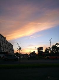 Cars on road by buildings against sky during sunset