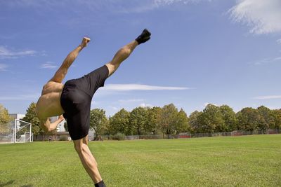 Shirtless man kicking on field against sky