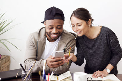 Happy male and female painters using smart phone at creative office