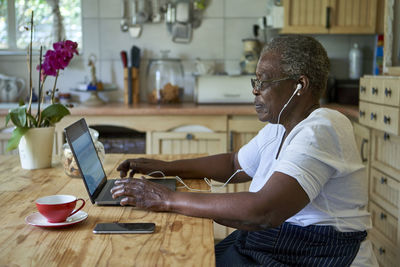 Senior woman sitting at kitchen table using laptop