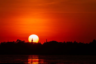 Silhouette trees by lake against romantic sky at sunset