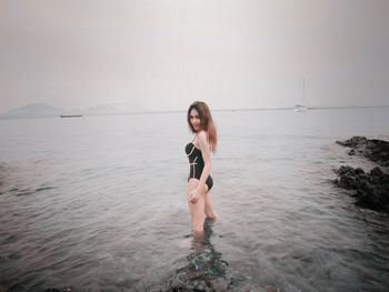 Portrait of young woman standing in sea against sky