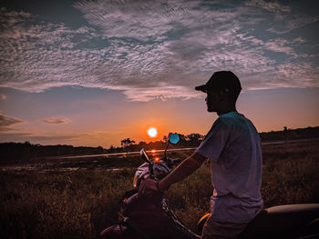 Man riding motorcycle on field against sky during sunset