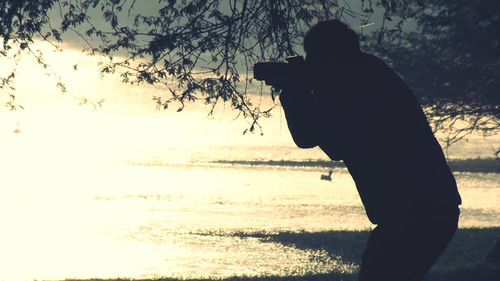 Silhouette man photographing at beach against sky during sunset