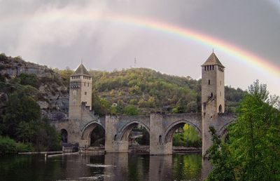 Arch bridge over river by building against rainbow in sky