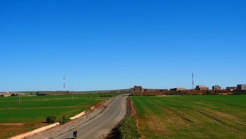 Road amidst field against clear blue sky