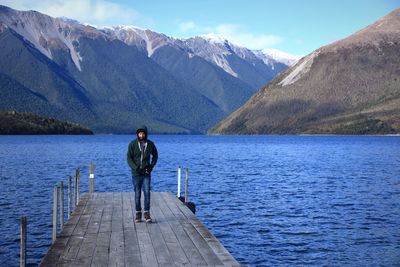 Young man walking on pier over lake against mountains