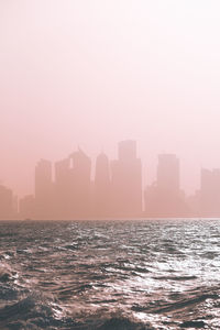 Sea by buildings against sky during sunset