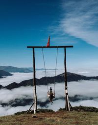 Woman enjoying swing at mountain peak against sky