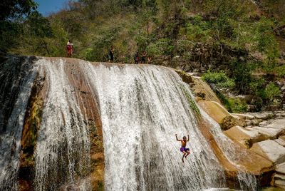People standing on rock formation by waterfall