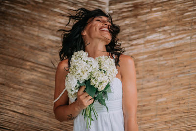 Young woman holding flower while standing against wooden wall