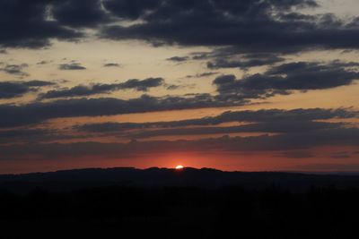 Silhouette landscape against dramatic sky during sunset