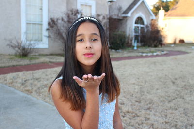 Portrait of girl blowing kiss while standing on footpath against house