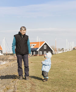 Grandfather with granddaughter standing on field against cloudy sky