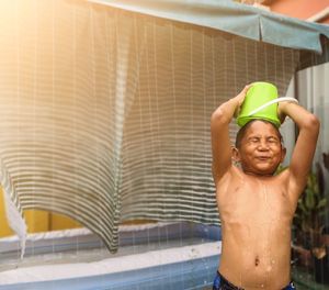 Smiling shirtless boy playing with water against house