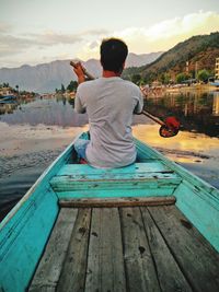 Rear view of man sitting on shore against sky