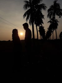 Silhouette people standing by palm trees against sky during sunset