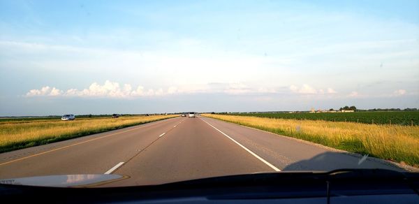 Road amidst field seen through car windshield