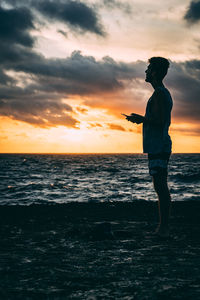 Silhouette man standing on beach against sky during sunset