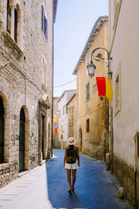 Rear view of woman walking on narrow alley amidst buildings