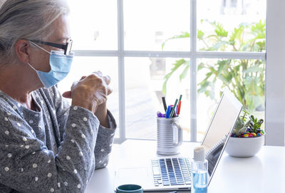 Side view of senior woman wearing mask looking at laptop