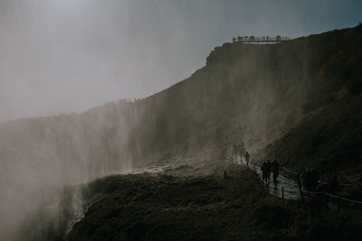 Scenic view of people walking on footpath by waterfall against sky