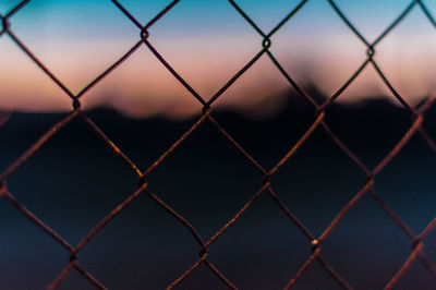 Full frame shot of chainlink fence against sky during sunset