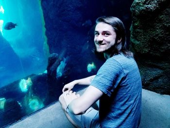 Portrait of smiling young woman sitting on rock in aquarium