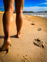 Low section of woman walking on sand at beach