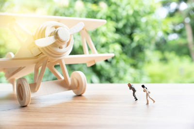Close-up of toy airplane with figurines on wooden table against trees