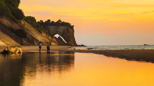 People on rock by sea against sky during sunset