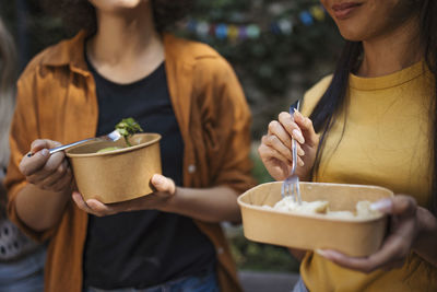 Happy friends eating together in garden from disposable containers