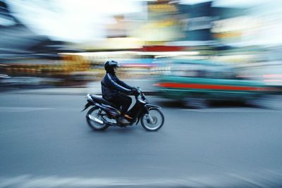 Blurred motion of man riding motor scooter on road