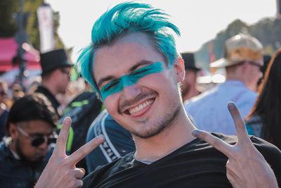 Close-up portrait of young man with dyed hair showing peace sign