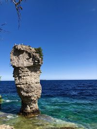 Rocks on sea shore against clear blue sky