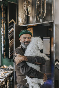 Portrait of smiling craftsman hugging pet dog in frame shop