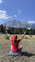 Rear view of woman with arms raised standing on mountain against sky