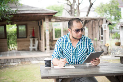 Man with disposable cup using digital tablet outdoors